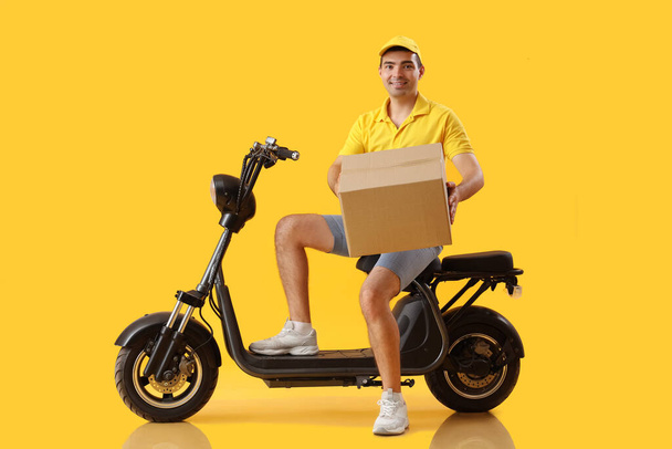Mannelijke koerier met pakket en fiets op gele achtergrond - Foto, afbeelding