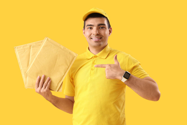 Άντρας κούριερ δείχνει φακέλους σε κίτρινο φόντο - Φωτογραφία, εικόνα