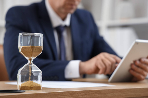 Hourglass on table of mature businessman in office, closeup - Photo, Image