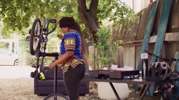 Африканские американские велосипедистки вносят коррективы в детали велосипеда с использованием профессиональных многоинструментальных инструментов на открытом воздухе. Здоровая черная женщина чинит велосипедное колесо и когсет. - Кадры, видео
