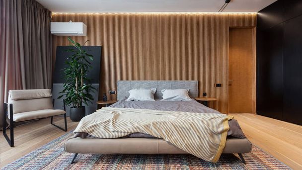 Moderni parvi tyyli makuuhuone asunnossa. Mukava parivuode vuodevaatteet ja minimalistinen nojatuoli vastaan puinen seinä. Rentoutua ja nukkua käsite - Valokuva, kuva
