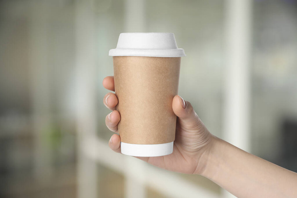 Coffee to go. Woman holding paper cup of hot drink on blurred background, closeup - Photo, image