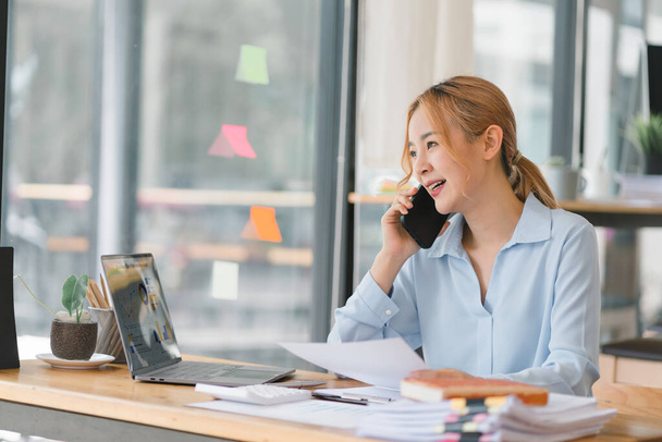 Young adult Asian businesswoman, secretary, sales manager, business consultant, engaging in a phone conversation with a client at the office - Foto, imagen