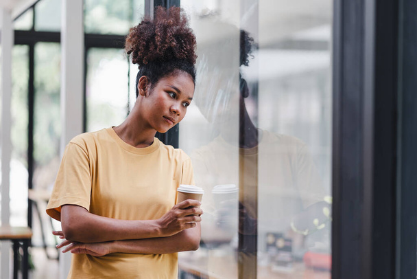 Afroamerikanerin mit Afro-Haaren, die aus dem Fenster schaut. Die frustrierte und verwirrte Frau wirkt unglücklich, wenn sie sich mit persönlichen Lebensproblemen auseinandersetzt - Foto, Bild