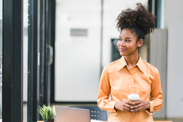 Portrait of successful and confident black businesswoman. A beautiful young African American woman, smiling at the camera while standing with her arms crossed in a modern office - 写真・画像