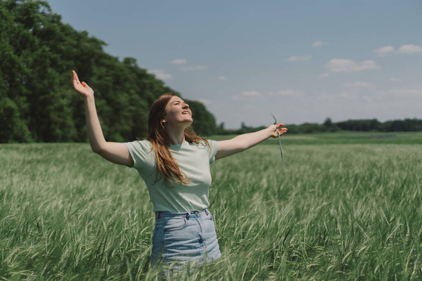 Una donna gode l'aria fresca nella natura in un campo di orzo verde. Campagna estiva e raccolta fiori. Atmosfera momento tranquillo - Foto, immagini
