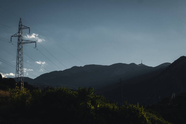 背景の山の上にテレビ塔が付いている前景の電極および木が付いている美しい風景. - 写真・画像