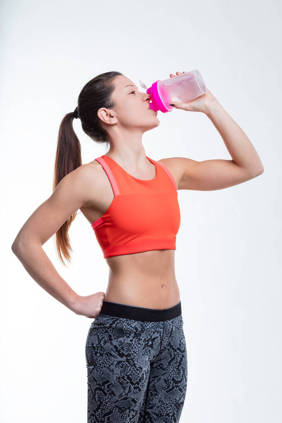 At the gym, a woman hydrates, her muscular arm on display, underscoring the importance of drinking water in achieving physical fitness - Photo, Image