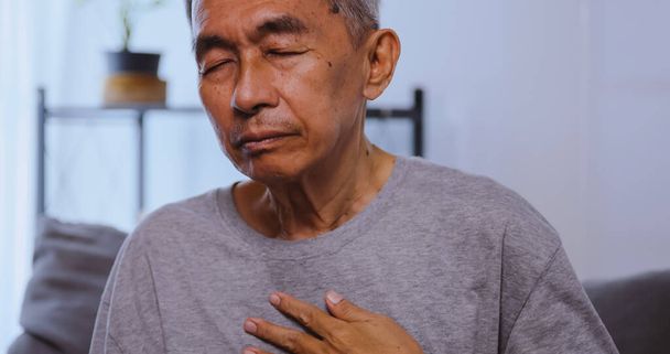 Азіатський старий має труднощі дихати, сидячи на дивані вдома. - Фото, зображення