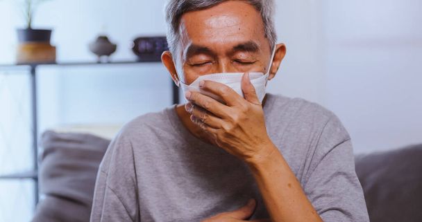 Ein älterer asiatischer Mann trägt eine Maske, während er an einer Atemwegserkrankung leidet. - Foto, Bild