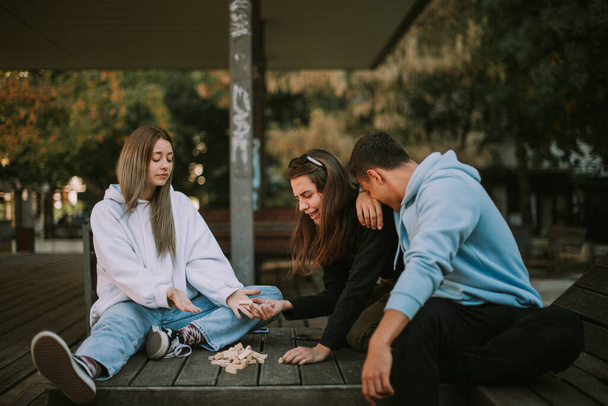 Tre amici che guardano il jenga sparso sulla panchina di legno - Foto, immagini