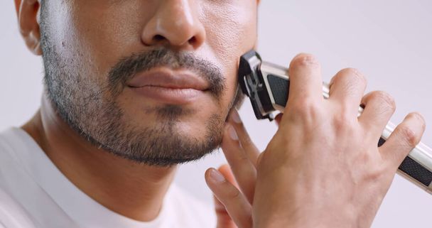 Un hombre está usando una afeitadora eléctrica para recortar el bigote y la barba mientras está de pie frente al espejo en el baño en casa. - Foto, imagen