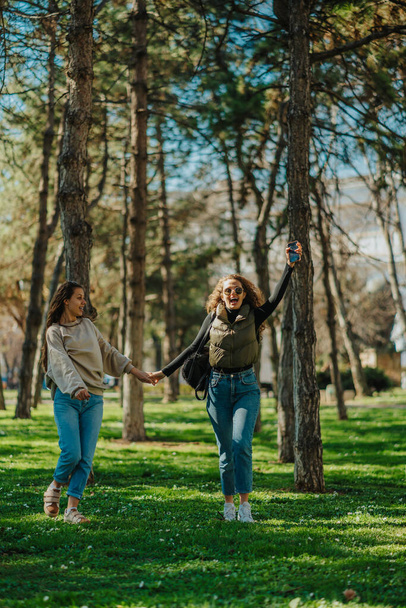 A lányok fogják egymás kezét, miközben a parkban lógnak. A barna lány a barátját nézi, ahogy sikoltozik. Elölnézeti felvétel - Fotó, kép