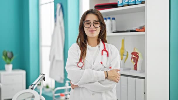 Młoda piękna Latynoska lekarz uśmiecha się pewnie stojąc z ramionami skrzyżowane gest w klinice - Materiał filmowy, wideo