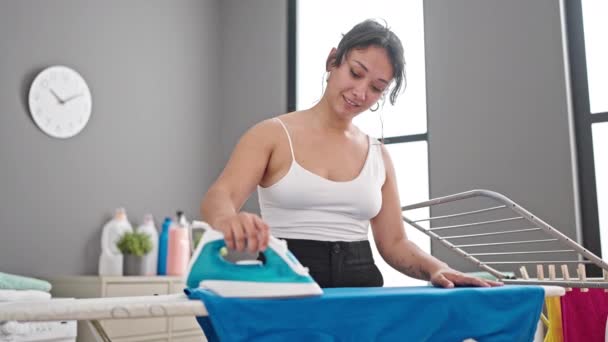 Young beautiful hispanic woman smiling confident ironing clothes at laundry room - Footage, Video