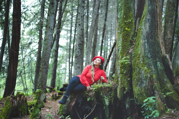 Mujer con actitud positiva sobre un tronco musgoso en medio del bosque. - Foto, imagen