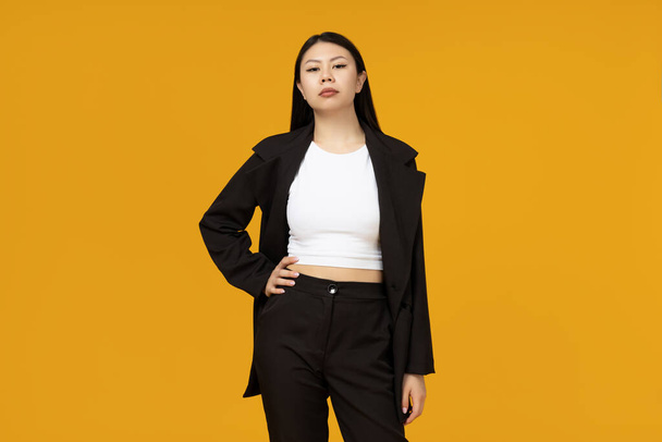 Ein seriöses asiatisches Mädchen im klassischen, strengen Stil auf gelbem Hintergrund - Foto, Bild