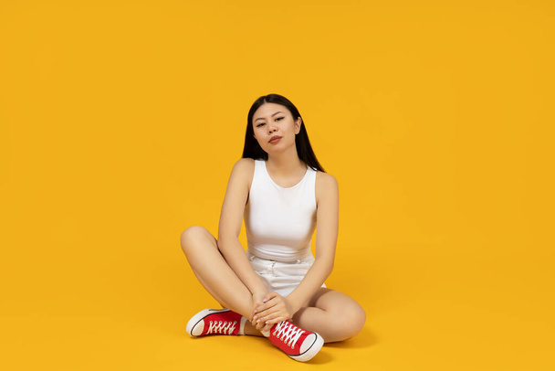 Krásná asijská dívka ve stylovém oblečení sedí na podlaze - Fotografie, Obrázek