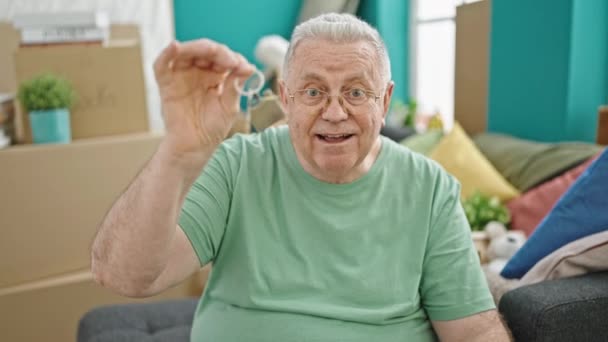 Középkorú ősz hajú férfi, akinek videohívása van, és új otthonában tartja a kulcsot. - Felvétel, videó