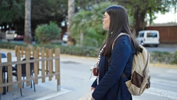 Молодая латиноамериканка-туристка в рюкзаке смотрит на карту города на улице - Кадры, видео