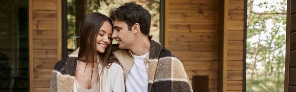 Cheerful romantic couple in blanket sitting with closed eyes near vacation house, banner - Photo, Image
