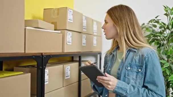 Nuori blondi nainen verkkokauppa liiketoiminnan työntekijä käyttäen kosketuslevy tarkistaa paketteja toimistossa - Materiaali, video