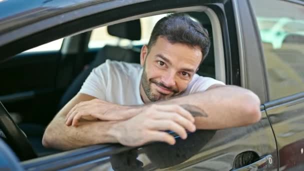 Молодий іспаномовний чоловік посміхається впевнено сидить на машині на вулиці
 - Кадри, відео