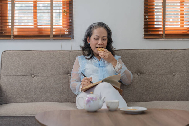 Mujer jubilada asiática feliz disfrutando leyendo libros y notas sobre el tema de la atención médica en el hogar relajado - Foto, Imagen