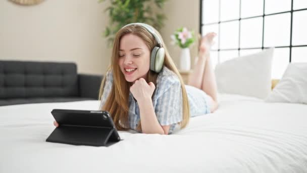 Mujer rubia joven viendo vídeo en touchpad acostado en la cama en el dormitorio - Metraje, vídeo