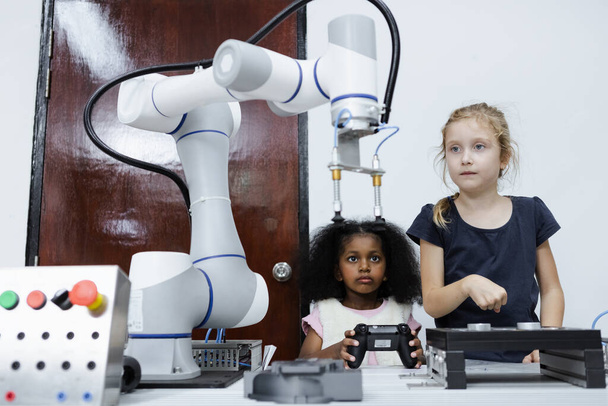 子供の女の子の原因と女の子アフリカ系アメリカ人教育教室でテーブルの上に電子ロボットアーム。未来のAIのための革新ロボット電子を学ぶ。システムスキルトレーニング。STEM教育の概念. - 写真・画像