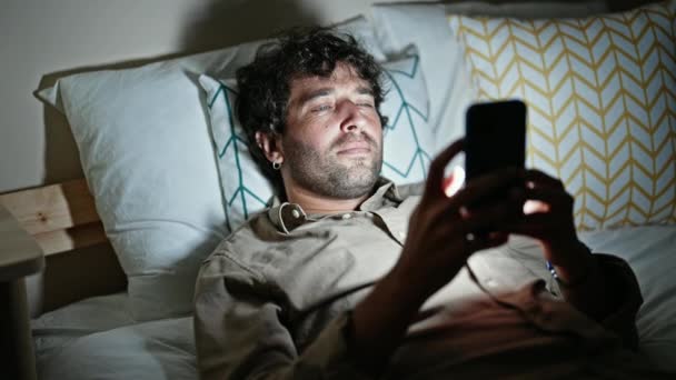 Junger hispanischer Mann schläft mit Smartphone müde im Schlafzimmer - Filmmaterial, Video
