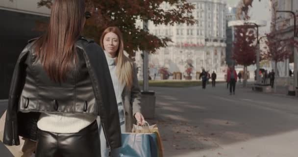 Meisjes ontmoeten elkaar in de stad na een shopping spree, zonnige herfstdag - Video