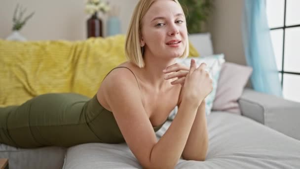 Young blonde woman smiling lying on the sofa at home - Footage, Video