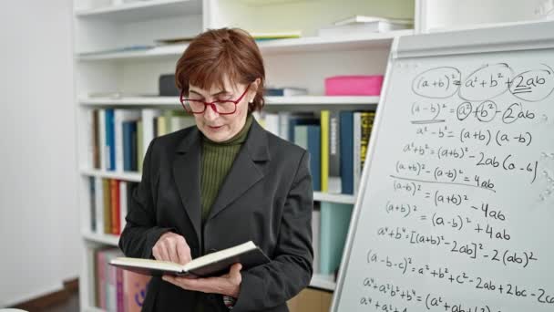 Mature hispanic woman teacher standing reading book at library university - Footage, Video