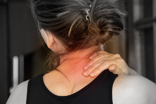 Ένα νεαρό κορίτσι κρατά το χέρι της στο λαιμό της από πόνο στην πλάτη στο σπίτι, πόνο στην πλάτη - Φωτογραφία, εικόνα