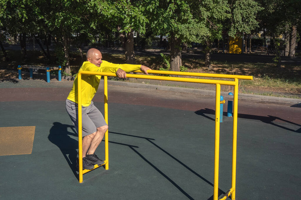 Man performs an exercise on parallel bars on a street sports ground on a summer sunny day. Healthy lifestyle - Photo, Image