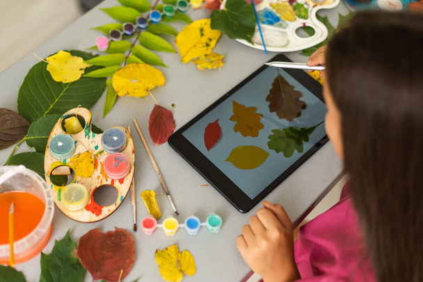 little girl artist paints autumn leaves . High quality photo - Foto, imagen