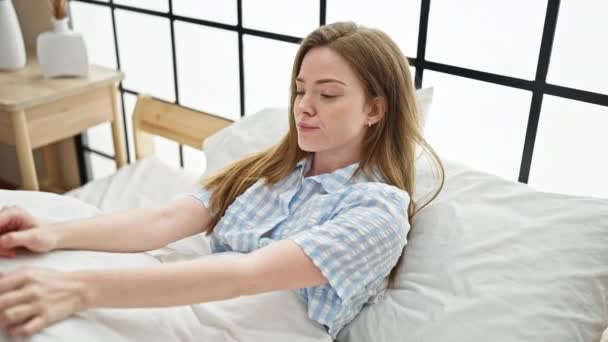 Jeune femme blonde se réveillant assise sur le lit dans la chambre - Séquence, vidéo