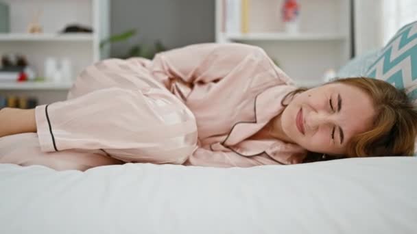 Nuori nainen kärsii kuukautiskivusta makaa sängyssä makuuhuoneessa - Materiaali, video