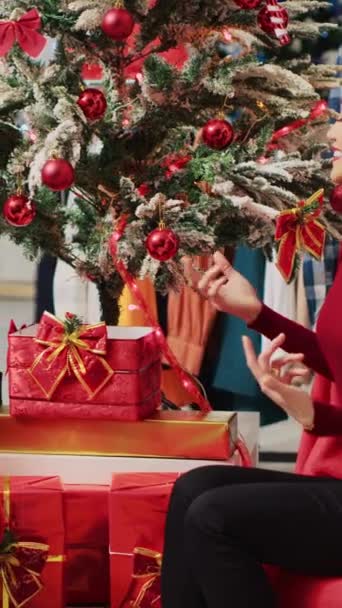 Video verticale Donna asiatica impegnata in una conversazione con il dipendente che impersona Babbo Natale durante la festiva esperienza di shopping natalizio. Cliente che riceve il regalo di Natale dal lavoratore nel negozio di moda - Filmati, video