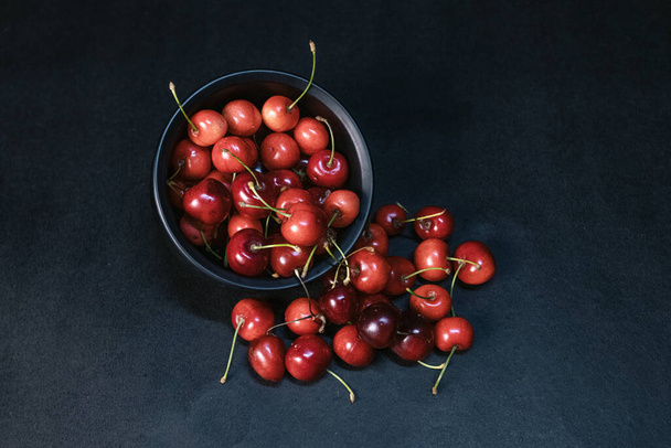 Sweet red cherries piled up in a black ceramic bowl on black background. Top view. Fruit Background. Selective focus. - Photo, Image
