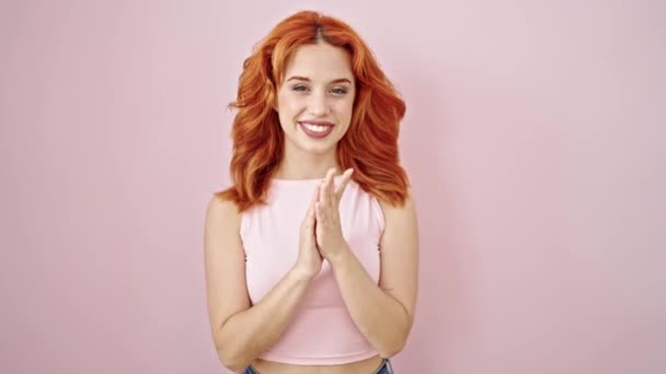 Νεαρή κοκκινομάλλα γυναίκα χαμογελά με αυτοπεποίθηση χειροκροτούν πάνω από απομονωμένο ροζ φόντο - Πλάνα, βίντεο