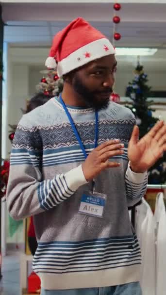 Vertical video Wife and husband in Christmas decorated shopping mall clothing store, being assisted by african american employee with finding perfect outfit during winter holiday season promotional - Footage, Video