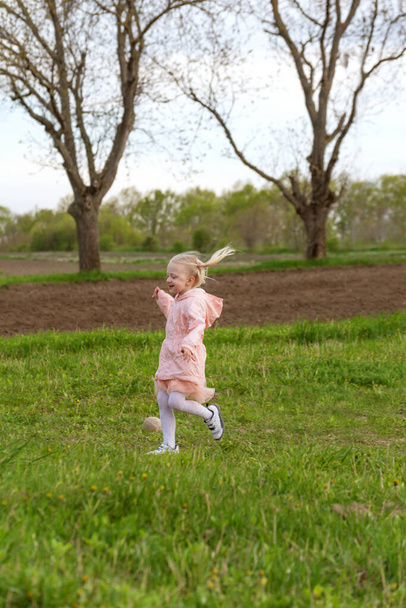 Correre bambina europea con i capelli biondi in abito rosa che corre attraverso il campo o prato. Telaio verticale - Foto, immagini