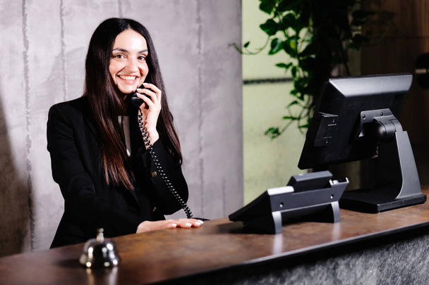 Otel resepsiyonisti. Çanı olan modern otel resepsiyonu. Otel tezgahında durup telefonla konuşan mutlu kadın resepsiyonist. - Fotoğraf, Görsel