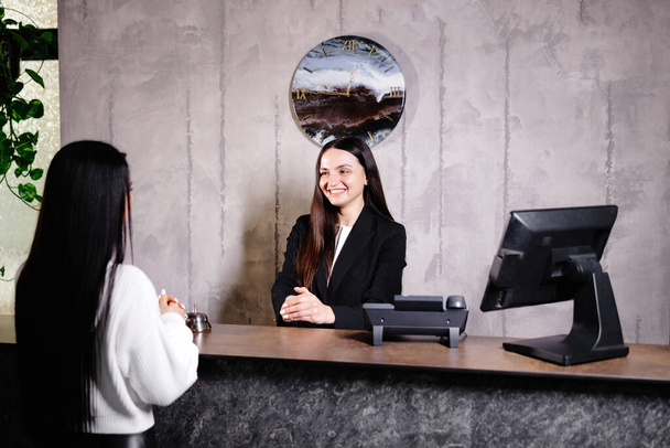 Amigável jovem concierge em pé atrás de um balcão de recepção conversando informações sala para os hóspedes de check-in em um hotel. - Foto, Imagem