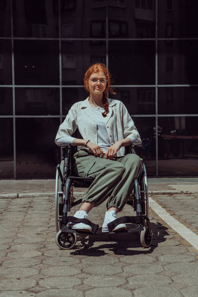 In front of a modern corporate building, a young woman sitting in a wheelchair confidently, symbolizing empowerment, inclusivity, and the strength to overcome challenges in the business world.  - Fotografie, Obrázek
