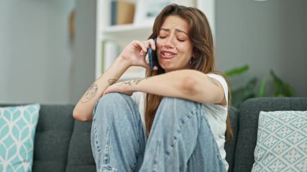 Junge schöne hispanische Frau sitzt auf dem Sofa und telefoniert mit dem Smartphone und weint zu Hause - Filmmaterial, Video