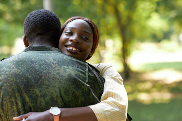 ハッピー アフリカ系アメリカ人女性 彼女の軍事的な夫を抱擁しながら,彼らは屋外に立っている - 写真・画像