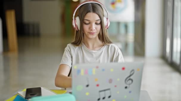 Jovem estudante bonita usando laptop e fones de ouvido estudando na biblioteca - Filmagem, Vídeo